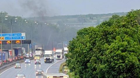 Cars and lorries travelling on the motorway with a fire visible in the background