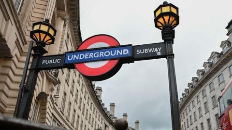 The entrance to a London Underground subway, with the red, whit ea blue Underground logo and yellow lamps.