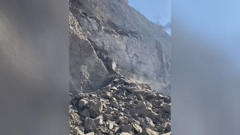 A huge pile of smashed rocks at the base of a grey crumbling cliff