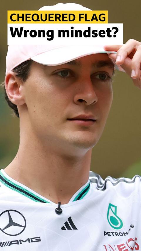 George Russell holds a hand to the visor of his pink Mercedes cap 