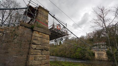 A complicated piece of scaffolding machinery has been set up between the two sides of a stone bridge to help rebuild it.