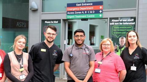 Ali Sidat stands outside a hospital entrance with a stethoscope around his neck, in the middle of a group of five colleagues.