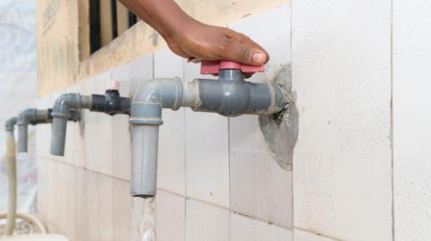 Hand turning red faucet tap, water pouring out of plastic faucet, West Africa
