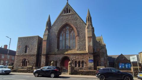 A red brick church on a sunny day with various cars parked in front of it