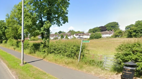 A green field with white houses in the distant background 