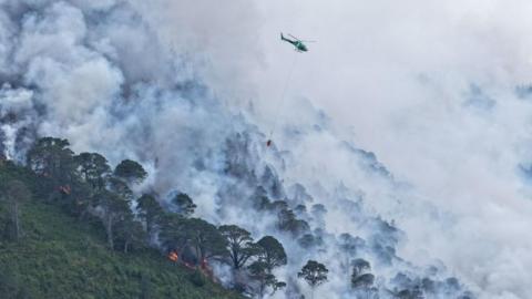 A helicopter waterbombs a large wildfire
