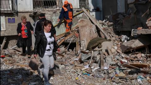 Two women - one wearing jeans and a leather jacket - walk near the rubble of an apartment block in Odesa