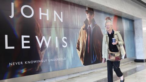 Elderly woman walks past John Lewis advertisement 