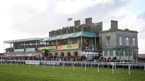 The main stand at Kelso racecourse with big crowds outside and a Scotland flag flying
