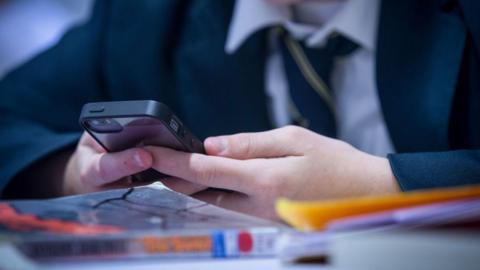 A child in school uniform holding an iPhone. 