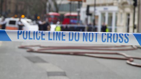 Police Line Do Not Cross tape against blurred city background - stock photo