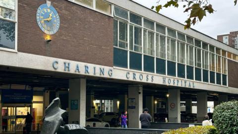 Charing Cross Hospital exterior shows blue signage, clock and patients beneath blue-clad windows