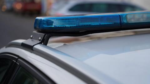 A close-up shot of the roof of a white police car with its blue and white lights, which are switched off.