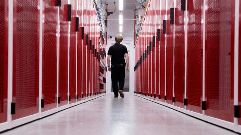 A worker at a data centre in Sydney, Australia, walking down the middle of two rows of red-faced computer servers