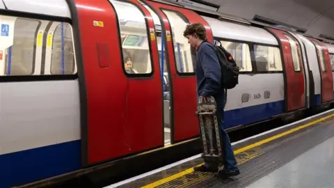 A person holding a skateboard gets on the tube