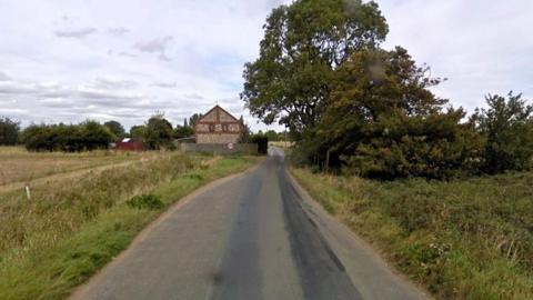 Google Image view of Station Road. A rural road with green fields either side and a house can be seen in the distance.  The proposed development was on the right hand side of the road. 