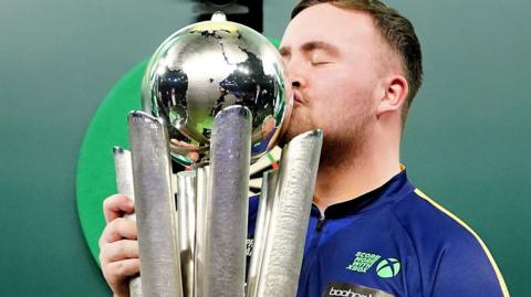 Luke Littler kisses the World Championship trophy