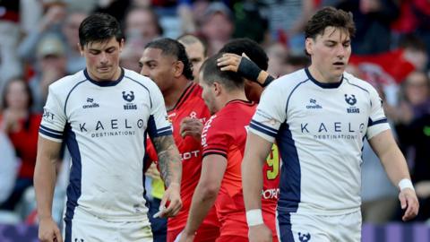 Louis Rees-Zammit (left) walks on the pitch with his head tilted down with Tom Jordan (right) walking next to him after a Toulouse try