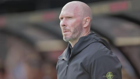 Shrewsbury Town boss Michael Appleton watches from the touchline in his gray club track top