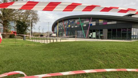 The Northern Gateway leisure park in the background, with a grassy area and red tape in the foreground