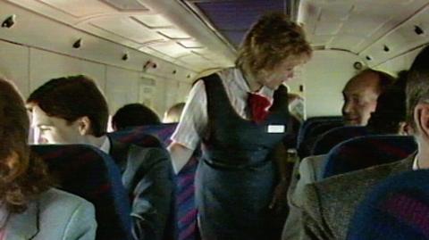 Air stewardess assisting passengers inside a small commuter plane.