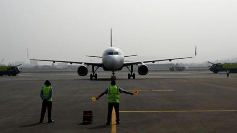 An airport ground crew standing on a runway in front of a white aircraft 
