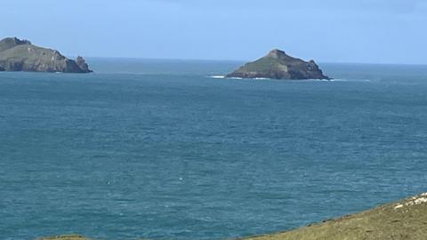 An expanse of sea towards a very small island and the headland alongside it 