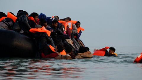 A group of people, all wearing life jackets, crowd onto an inflatable boat in the English Channel.