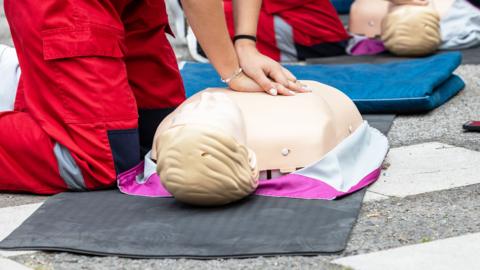 A person has both hands on a CPR doll on the floor