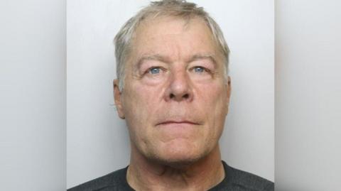 Headshot of a man with grey hair and blue eyes. He is wearing a black T-shirt.