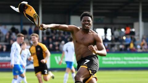 Bobby Kamwa jumps bare-chested in celebration after scoring a vital goal and holds his shirt in his right hand