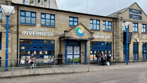 A straight on view of the entrance to the Inverness Bus station building. A sign on the the building says "welcome to Inverness", "Failte Gu Inbhir Nis" and there is also a Stagecoach sign above the door.