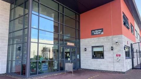 A school building with a large glass frontage and a brick and red frontage next to it.