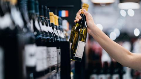 A woman reaches for a bottle of white wine off a supermarket shelf