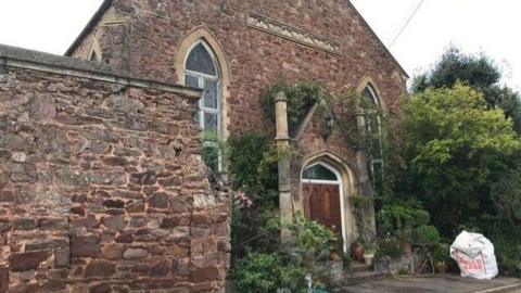 An exterior view of the chapel building showing plants and decorative windows