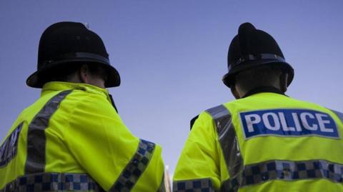Two police officers stood looking away from the camera.