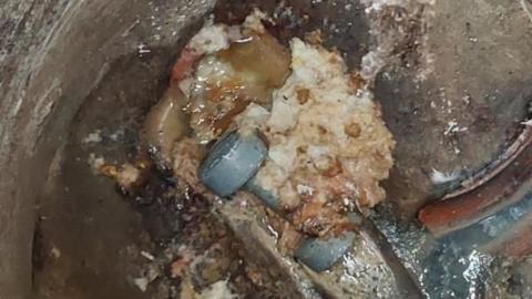 A gym weight in  a sewer with an enormous glob of fat attached