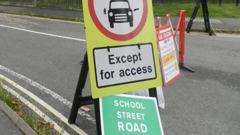 Street signs that read "No Parking. School zone", "Except for access" and "School street road". They are placed in a middle of a road.