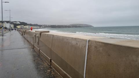 The wall, which is a beige, thick concrete structure, with Onchan head in the distance.