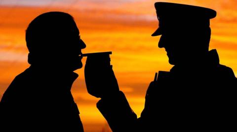 A silhouette showing a man stopped by police receiving a breath test on a breathalyser. 