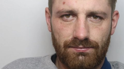 Krzysztof Orzechowski's mugshot. He has a brown beard and short hair. He is wearing a grey prison-issue jumper and a blue prison-issue T-shirt.