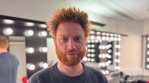 Joe Murphy in the dressing room of the Birmingham Rep with bright lights fringing mirrors behind him