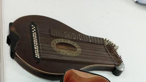 The harp is a dark brown colour with a decorative opening in the body of the instrument. There is a neck at the top of the instrument like there would be on a guitar. There are tens of strings beneath this. 