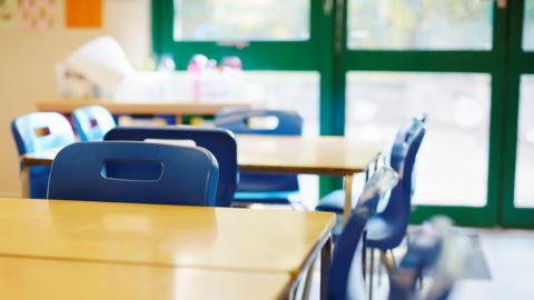 Close up of desks in a classroom with blue plastic chairs spaced around the table