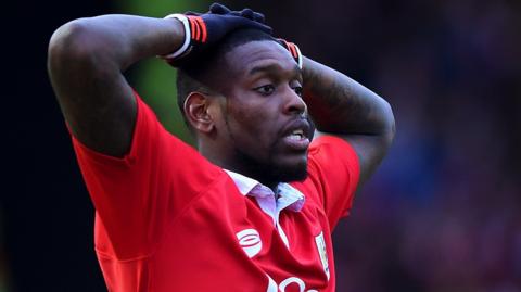 Jay Emmanuel-Thomas, wearing a red Bristol City shirt, has his hands on his head. He is wearing gloves.