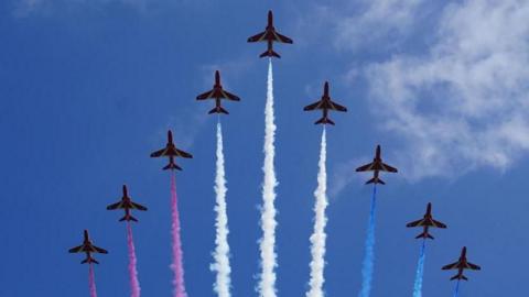 Nine red arrows are seen in formation, leaving trails of red, white and blue vapour, during a display in the sky