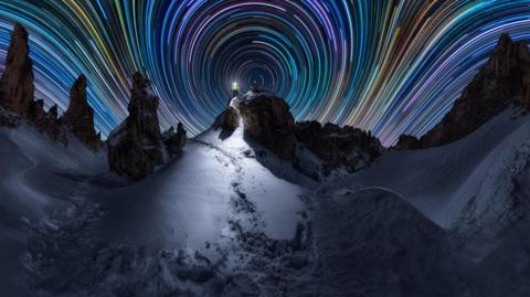time lapse photo showing snowy landscape with brightly coloured stripes in the night sky