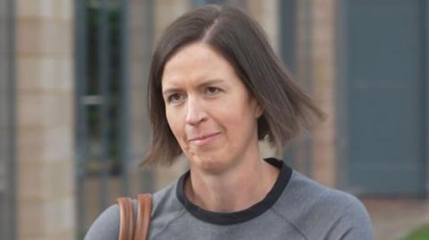 Dr Kate Searle arrives for a hearing at a tribunal - she is wearing a grey top, has a brown handbag over their shoulder and has brunette hair