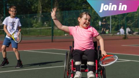 Two children playing tennis, including a girl in the foreground in a wheelchair.