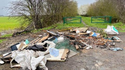A pile of mixed and burnt rubbish has been fly-tipped and left down a country lane.